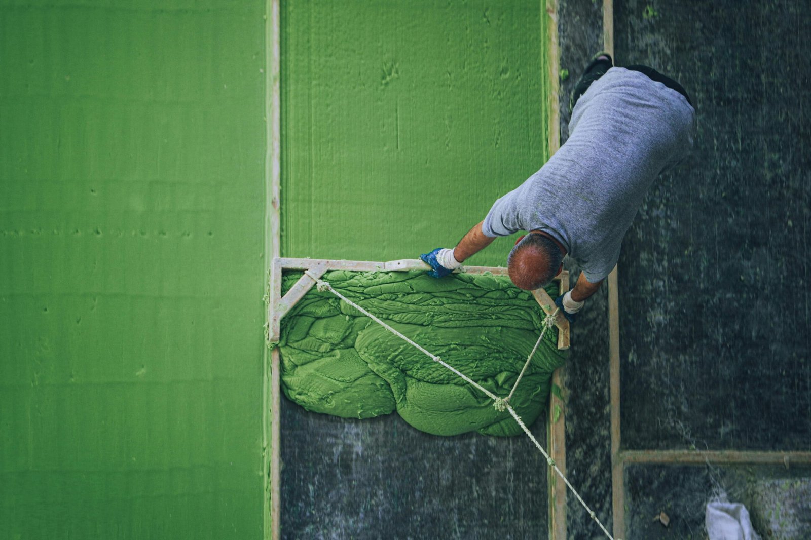 Aerial view of a construction worker spreading green cement mix on a surface.