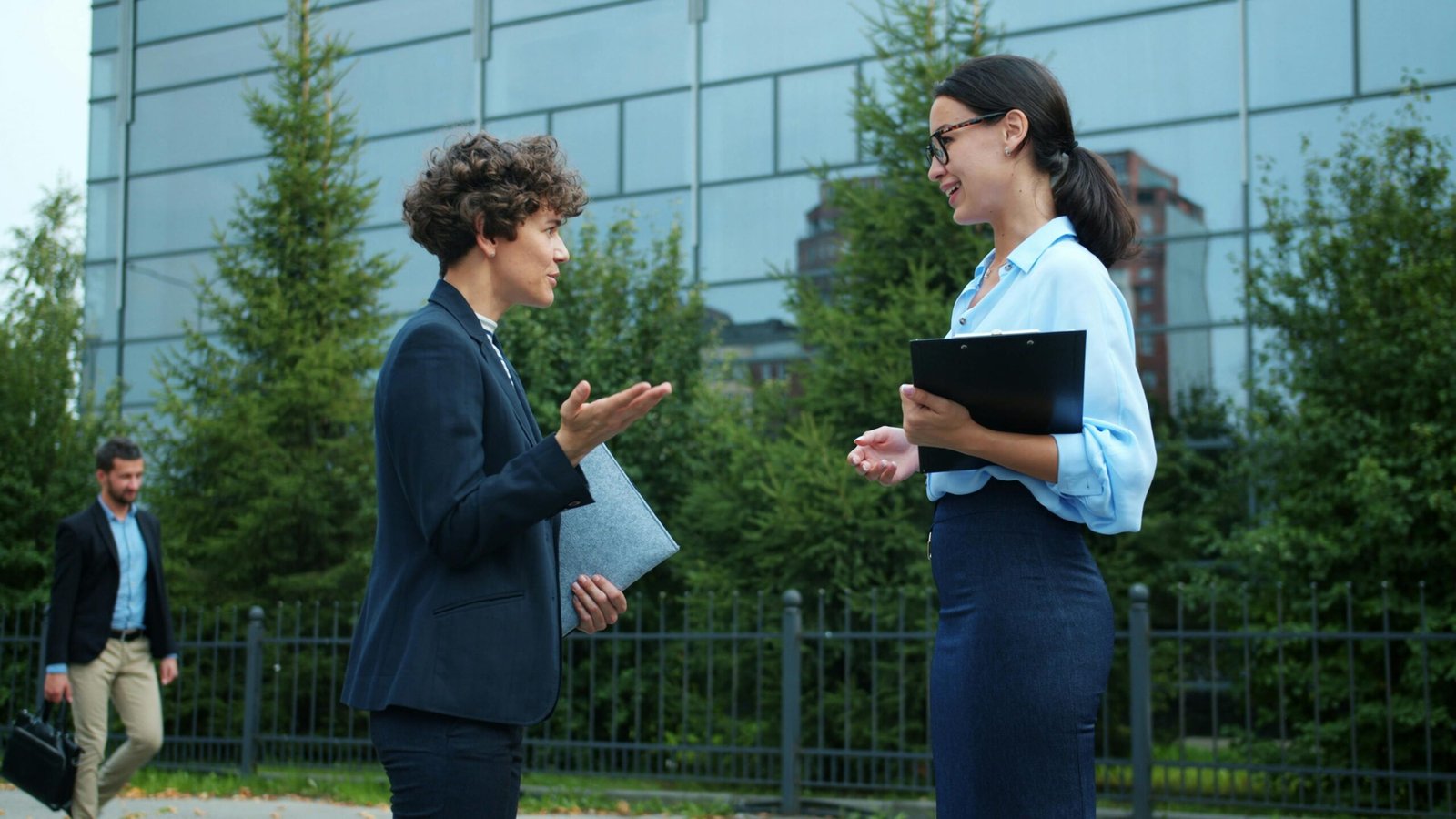 Two professionals having a discussion outdoors near office buildings.