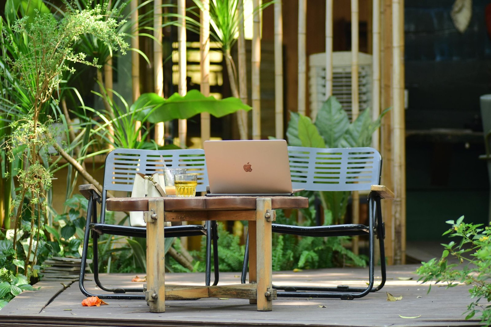 Stylish outdoor workspace with a laptop, table, and bench surrounded by greenery and natural elements.