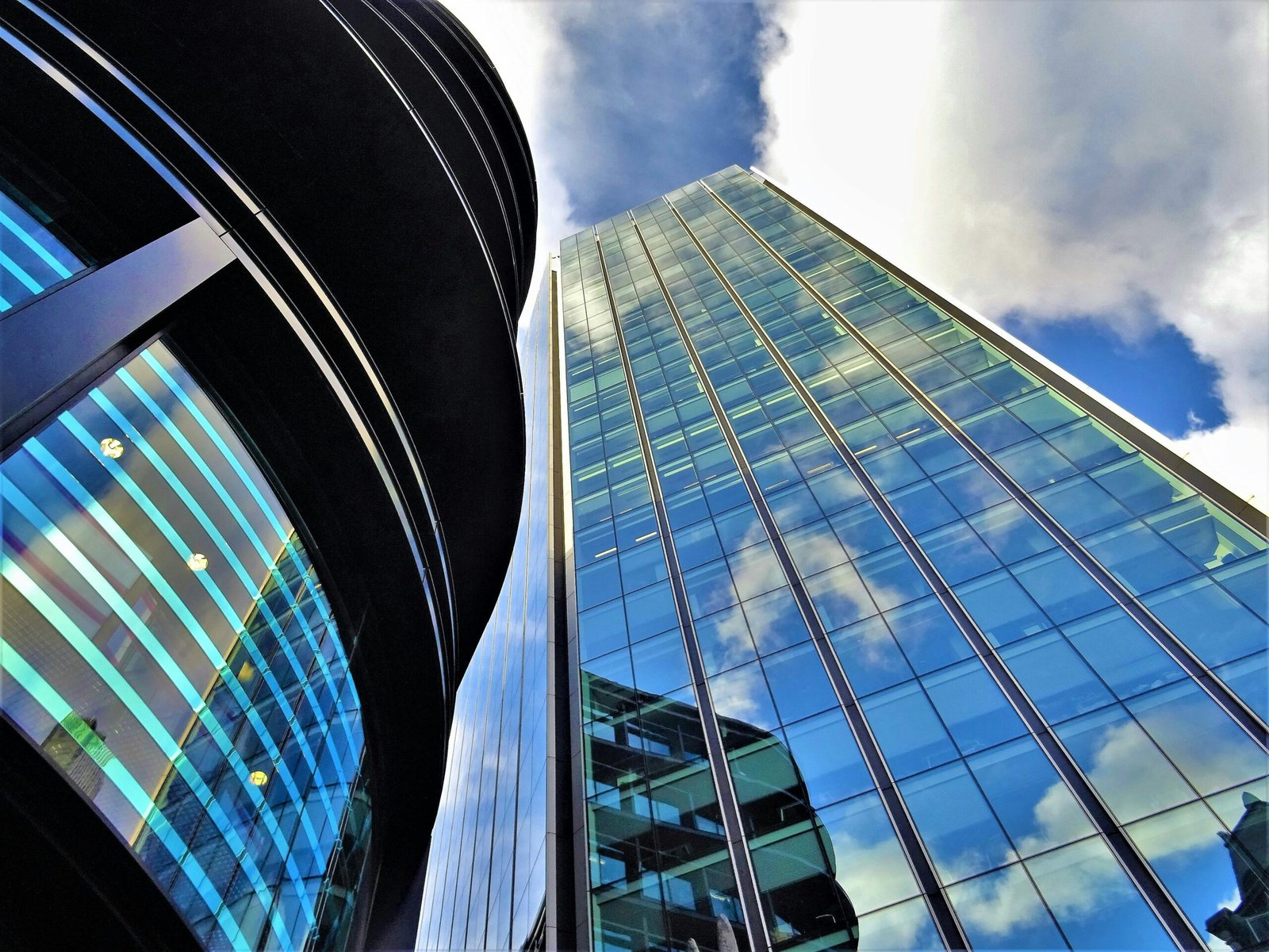 Low angle view of modern glass buildings with blue skies and clouds reflected in windows.